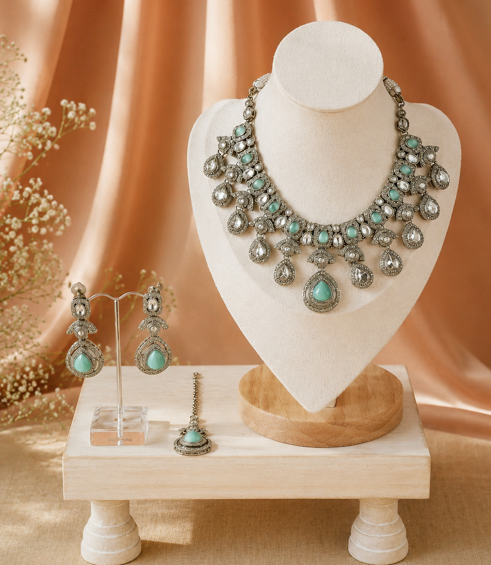 Jewelry set with necklace, earrings, and bracelet on a decorative stand against a soft peach background.